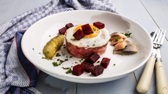 labskaus, north german specialty made with potatoes, beetroot, sour herring, gherkin slices, fried egg and parsley on a fine dining plate